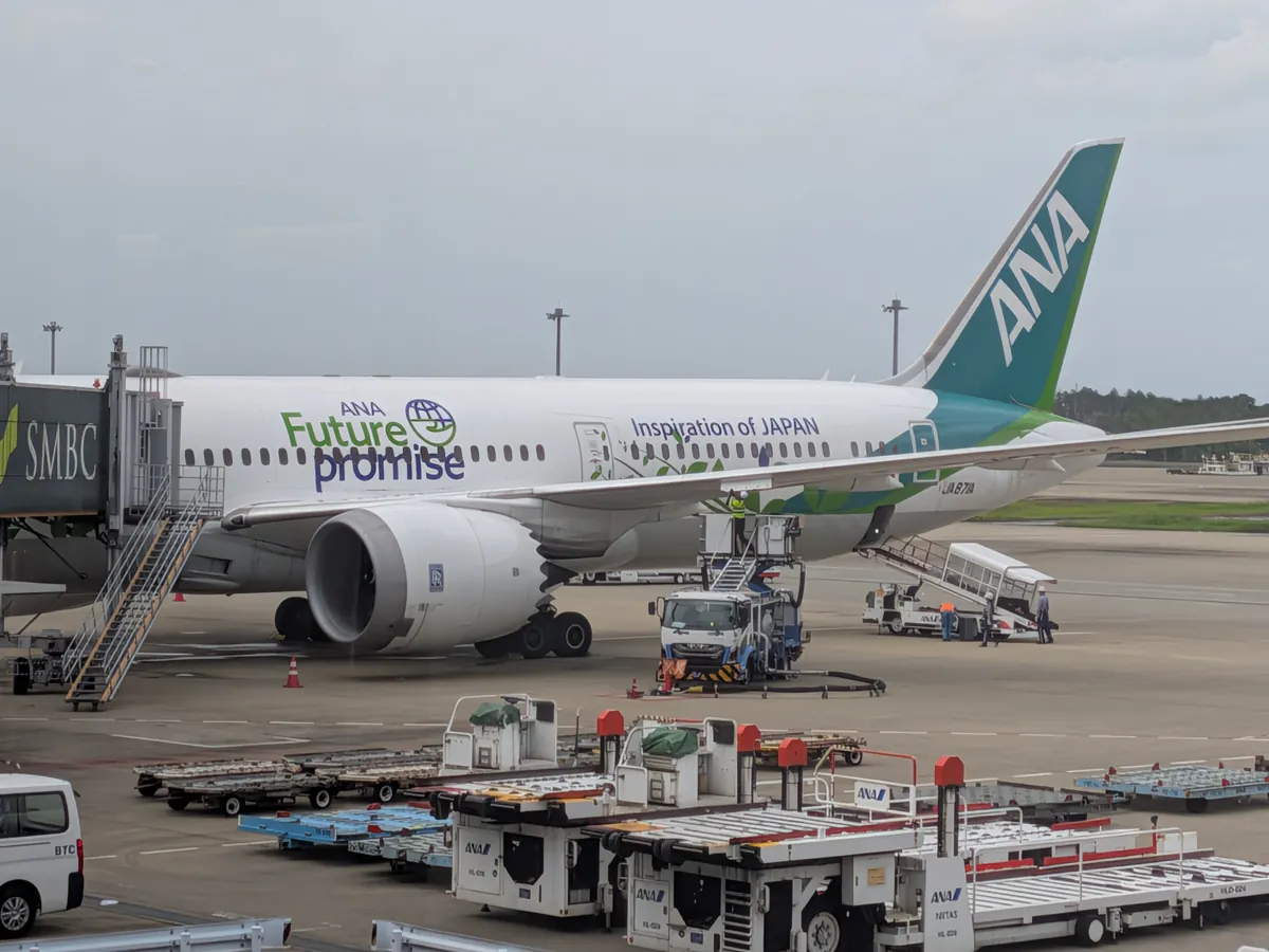 飛行場に駐機しているANAの特別塗装機「Future Promise」。緑色のデザインが施された機体にボーディングブリッジが接続され、周囲には作業車両が見える。