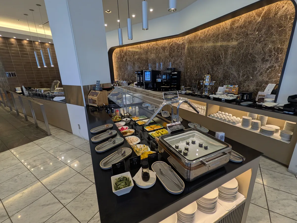 ラウンジ内の広々としたビュッフェカウンターの全景。様々な料理が並べられており、奥にはドリンクサーバーも見える。