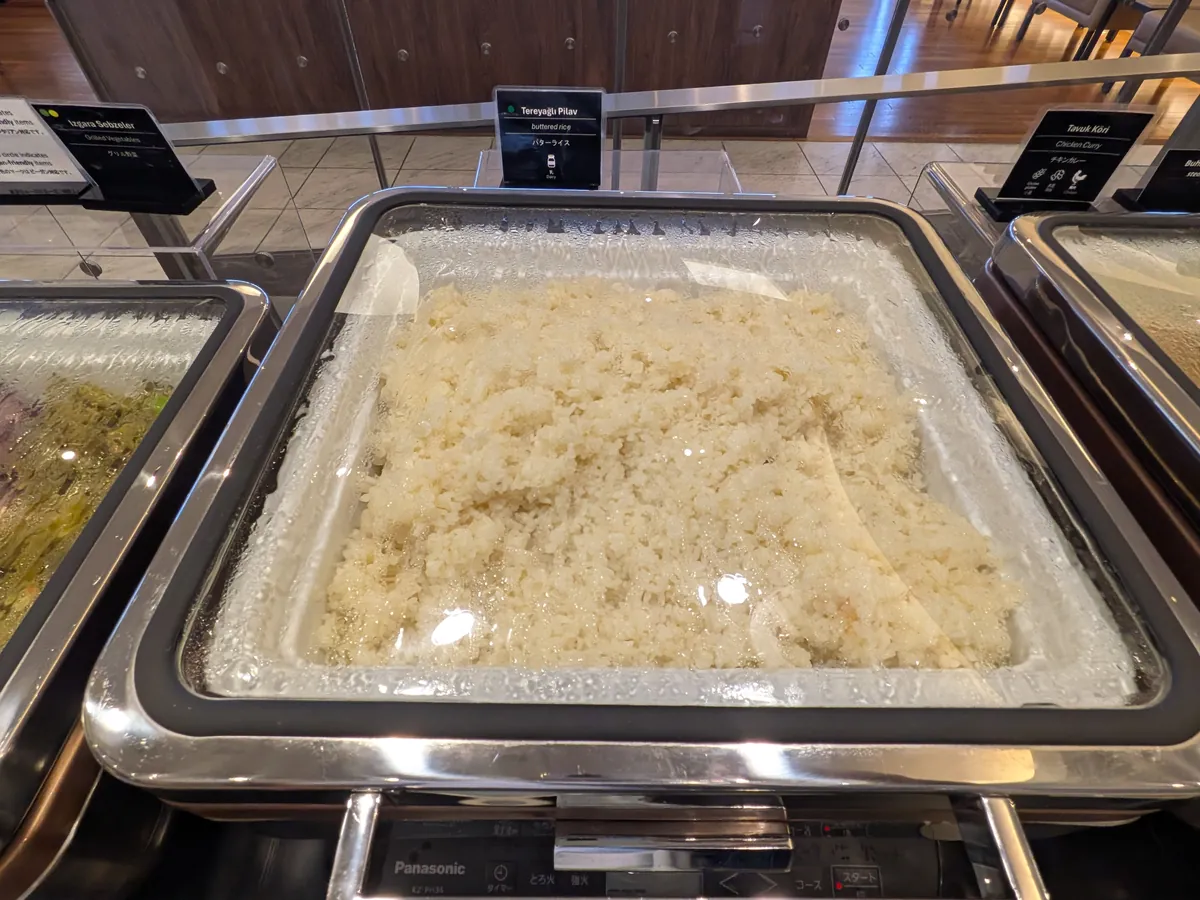 ビュッフェカウンターの温菜コーナーにある、蓋付きの保温器に入ったピラフ。湯気で蓋が曇っている様子がうかがえる。