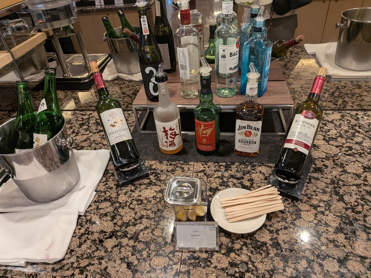 ラウンジのアルコール飲料コーナー。ワイン、ウイスキー、ジンなどのボトルが並び、カクテル用のレモンやマドラーも用意されている。