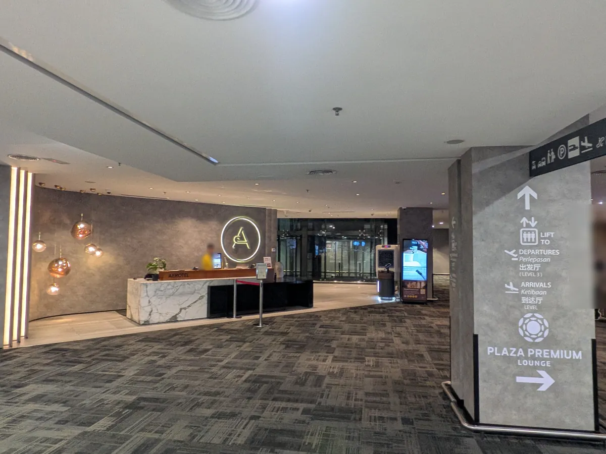エアロテル クアラルンプールのフロントロビー全景。銅色のペンダントライトとPLAZA PREMIUM LOUNGEの案内柱