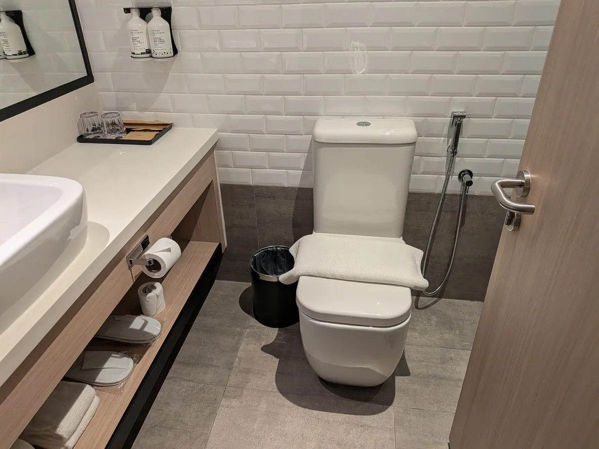 白いサブウェイタイルのバスルーム。トイレとハンドシャワー、スリッパとタオル