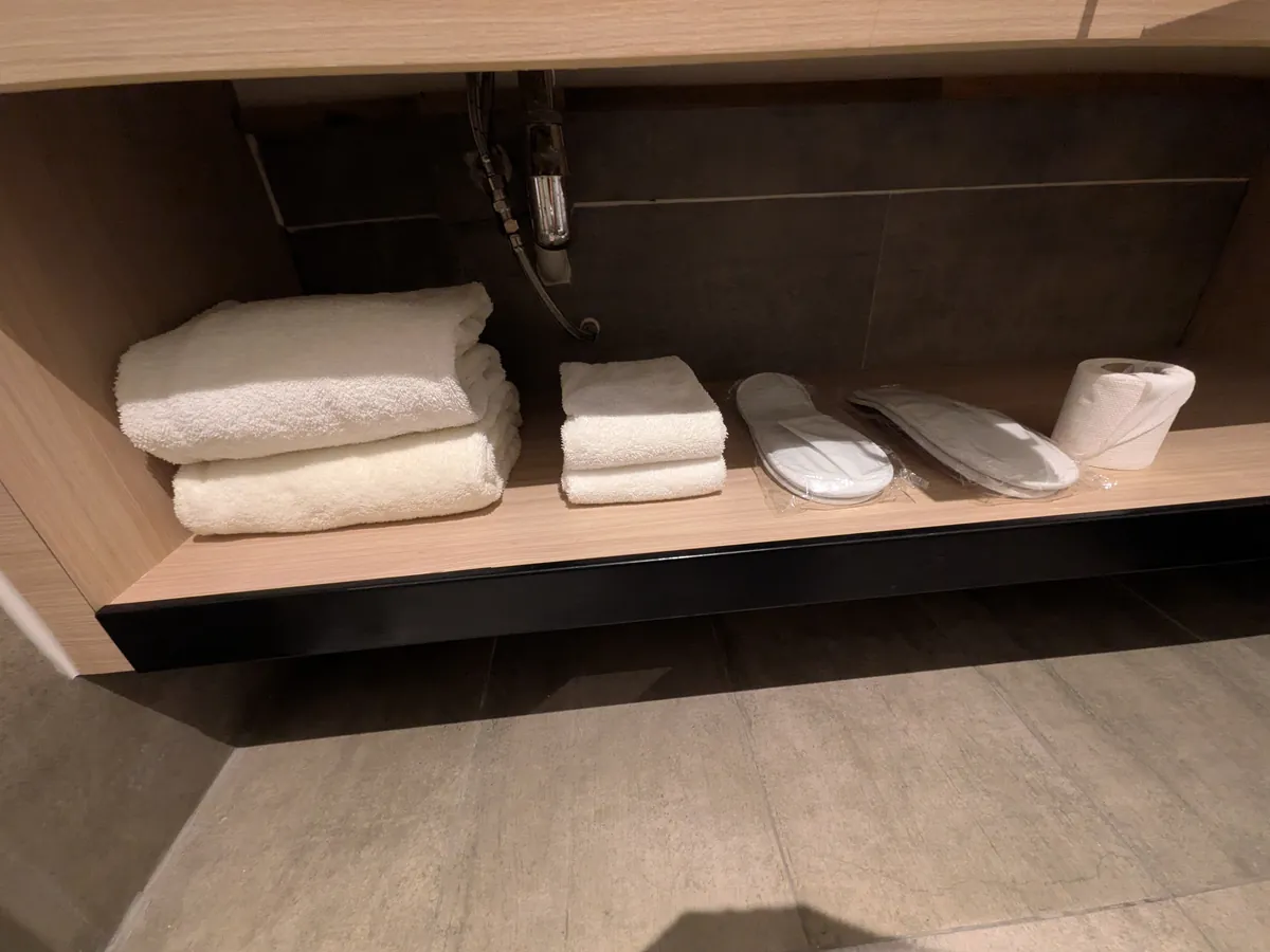 洗面台下の棚に並ぶバスタオル、フェイスタオル、スリッパ、予備のトイレットペーパー