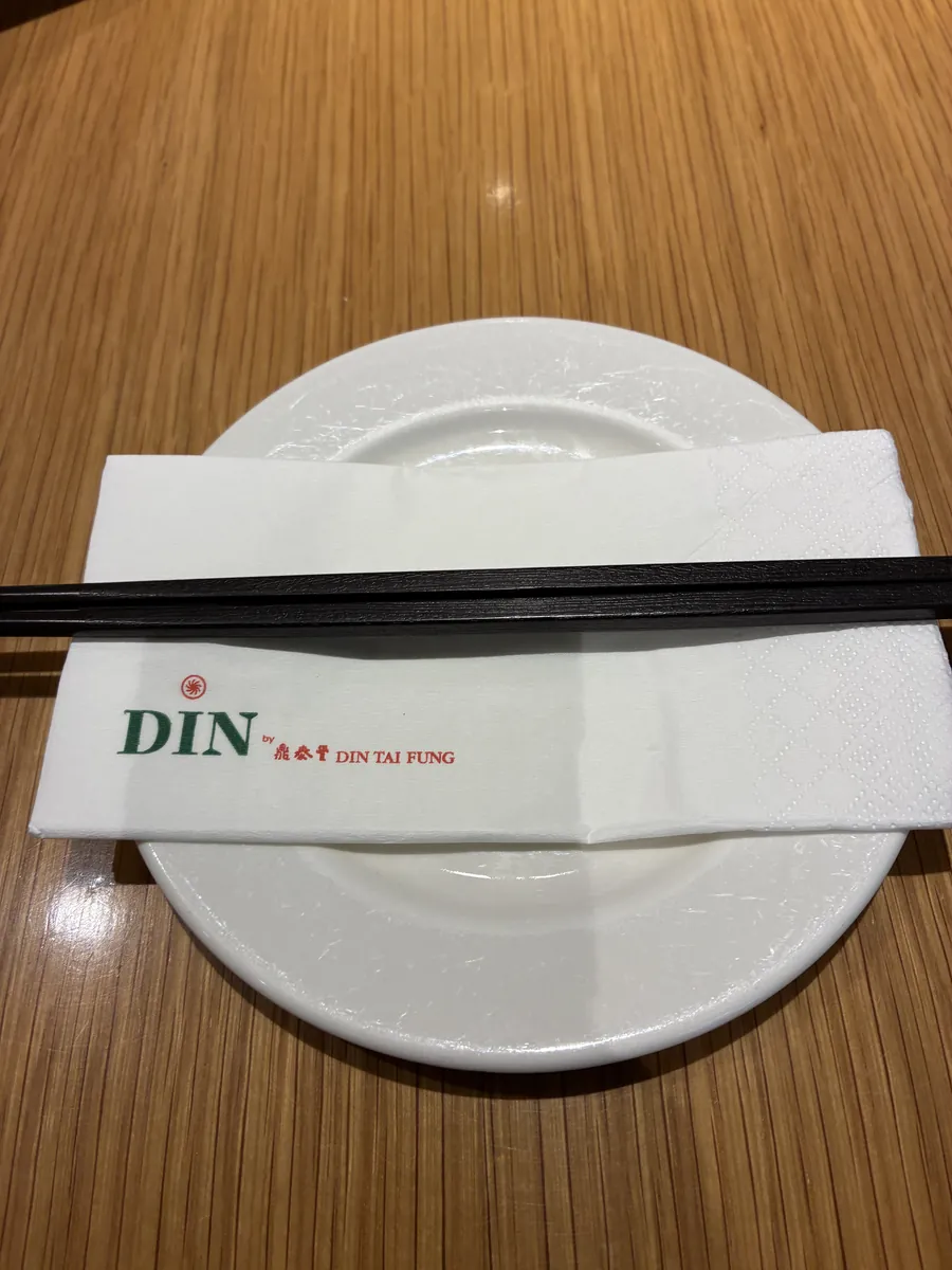 テーブルセッティング。白い取り皿の上にDIN by 鼎泰豊のロゴ入りナプキンと黒い箸