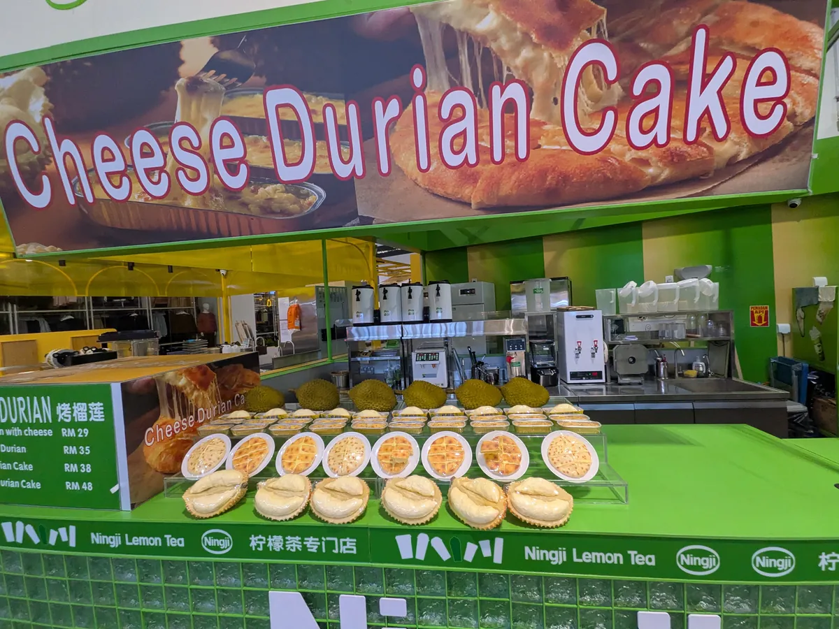 Cheese Durian Cakeの専門スタンド。カウンターにドリアンが並び、焼きドリアンケーキが陳列されている