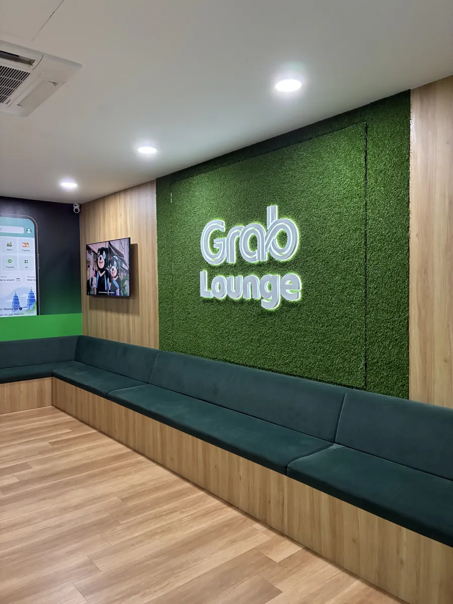 Grab Loungeの内観。人工芝の壁に光るGrab Loungeのロゴと、木目の壁沿いに続く深緑のベンチシート