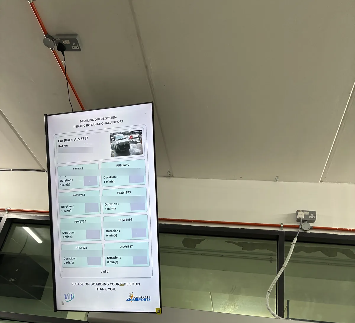 ペナン国際空港の配車乗り場に吊るされたE-HAILING QUEUE SYSTEMの電光掲示板。入構した車のナンバープレートと待機分数が一覧表示されている