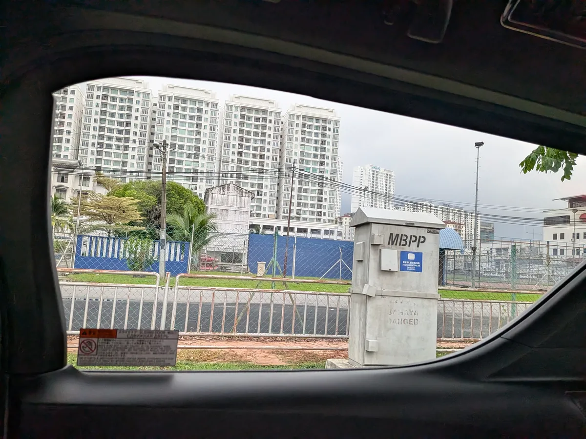 アルファードの車窓から見たペナンの街。手前に電力設備、奥に真新しい高層コンドミニアムが並ぶ。窓枠には日本語の注意書きシールが残っている