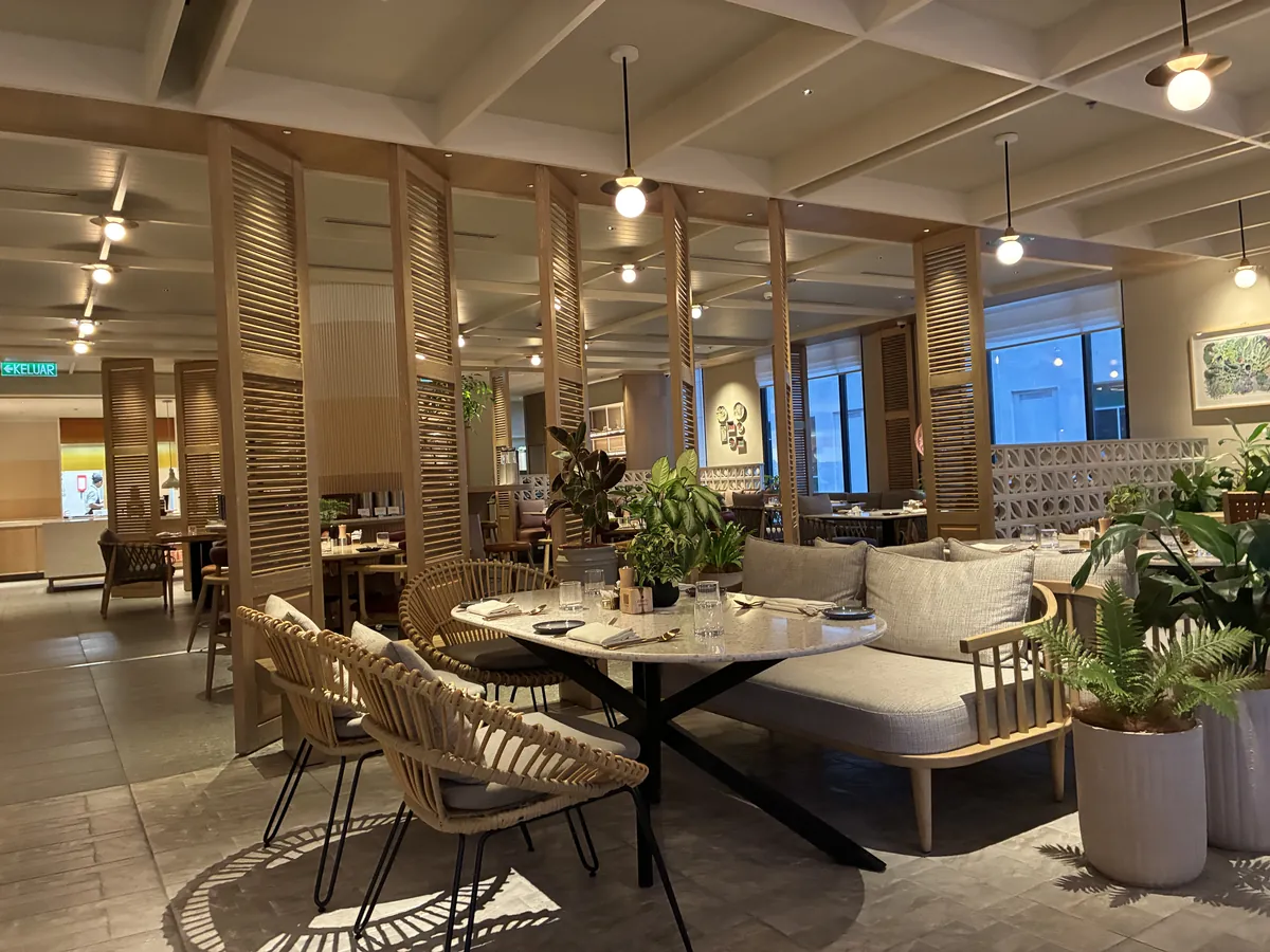 ザ・ミレン・ペナン2階のレストラン、リリの夜の店内。木のルーバーとラタンチェア、鉢植えの緑が並ぶ