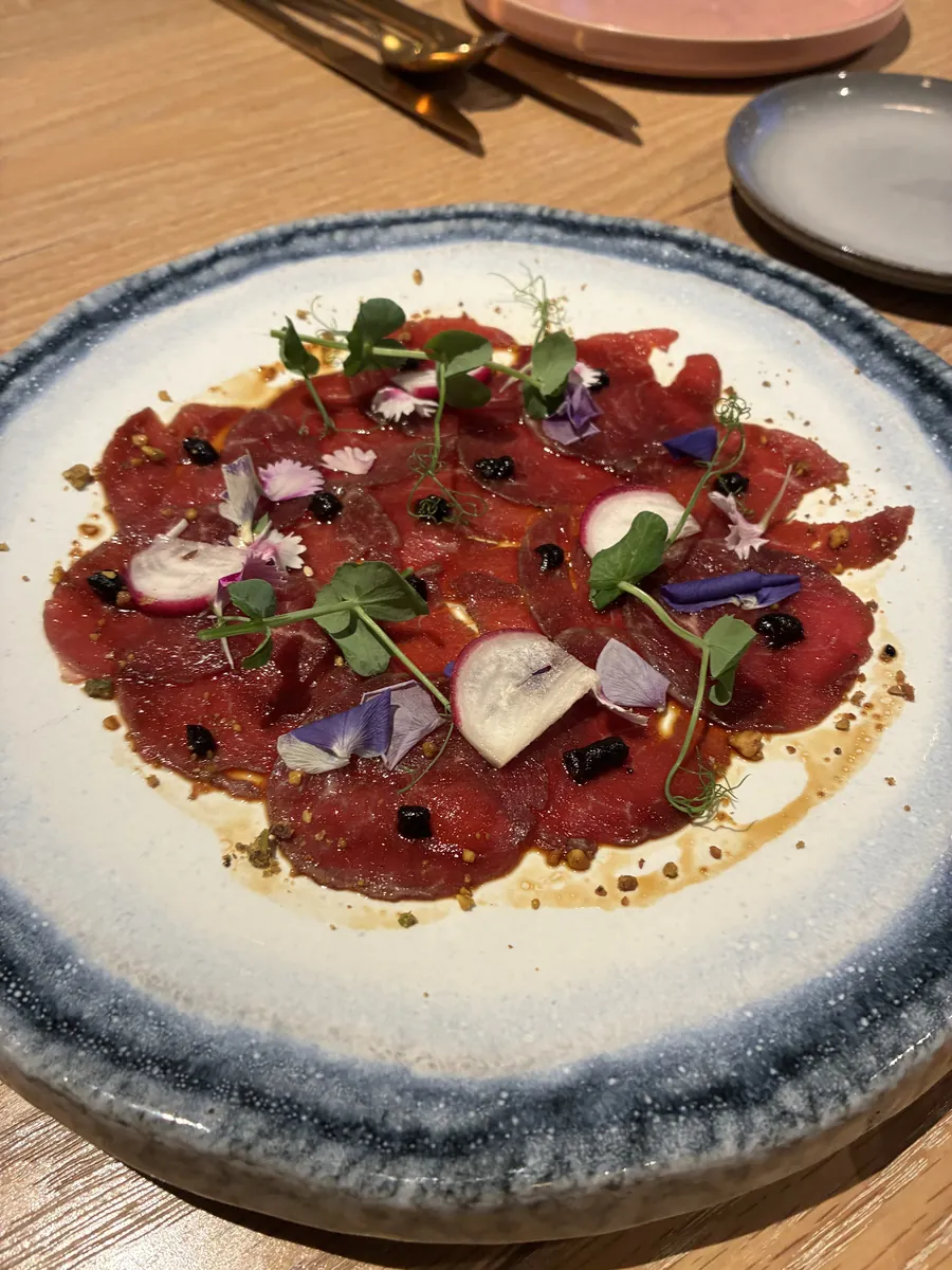 牛肉のカルパッチョ。マッシュルームとエディブルフラワー、オリーブが散らされている