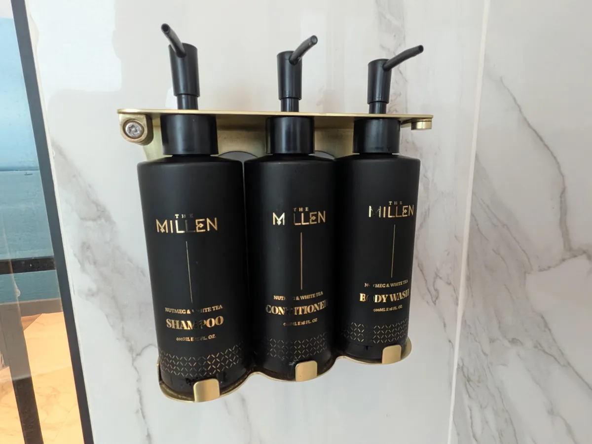 壁掛けのバスアメニティ。THE MILLENのロゴが入った黒いボトルが3本並ぶ