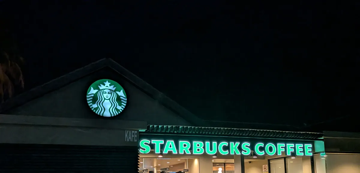 ビーチのそばにあるスターバックスの夜の外観。切妻屋根のロゴサインと緑に光るSTARBUCKS COFFEEの看板