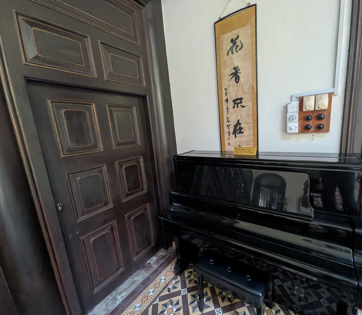 黒いピアノと中国の掛け軸、幾何学模様のタイル床が同居する館内の一角