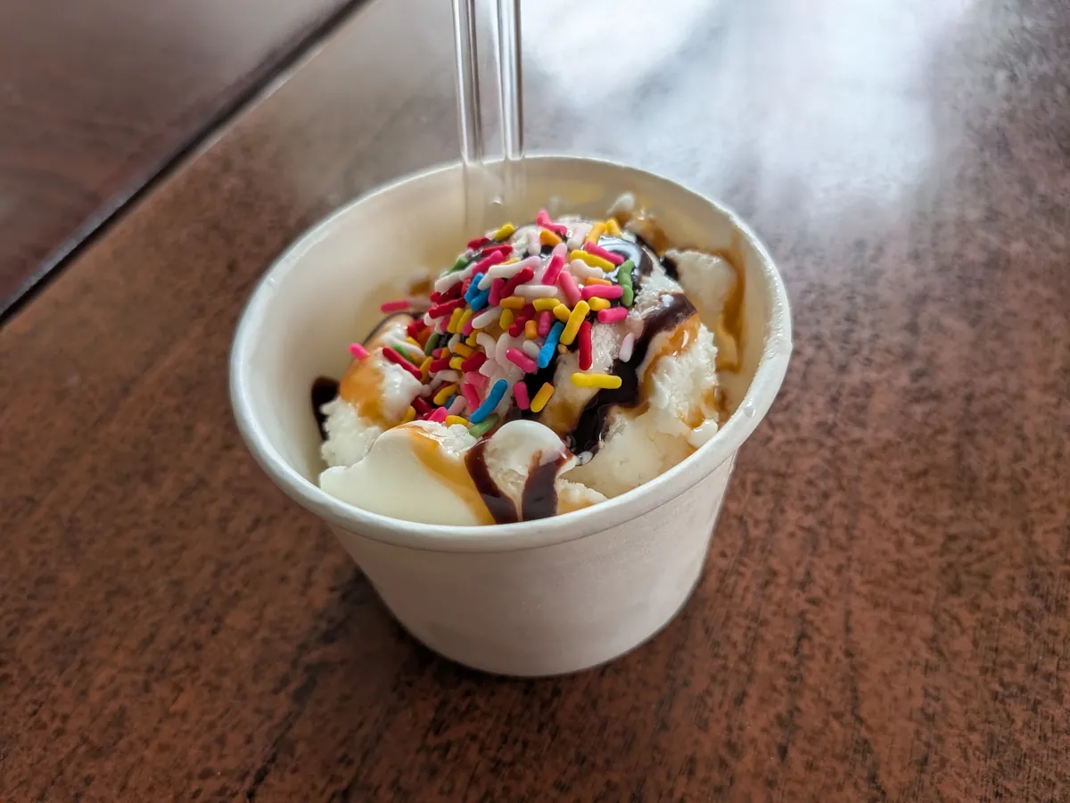 キッズセットのデザート。紙カップのバニラアイスにチョコとキャラメルのソース、カラフルなスプレーがかかっている