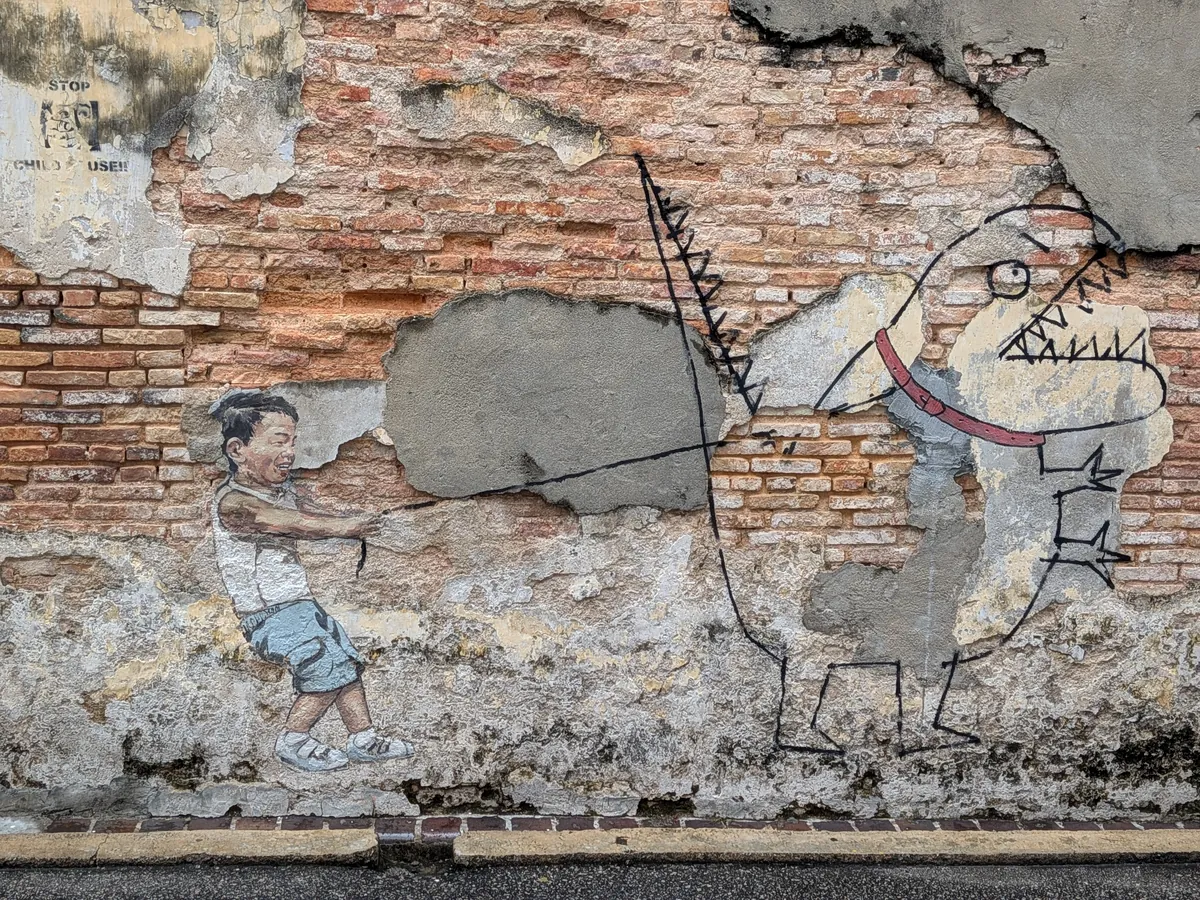 リアルに描かれた男の子が線画の恐竜を引っぱる壁画。恐竜の体は壁の剥がれたセメント部分と重なっている