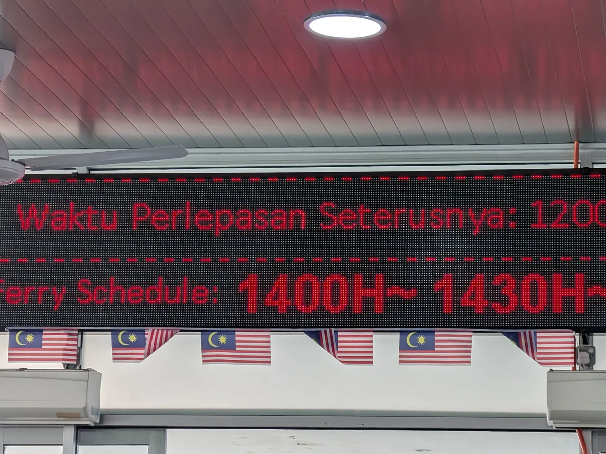 電光掲示板のアップ。Waktu Perlepasan Seterusnyaの表示とマレーシア国旗の飾り