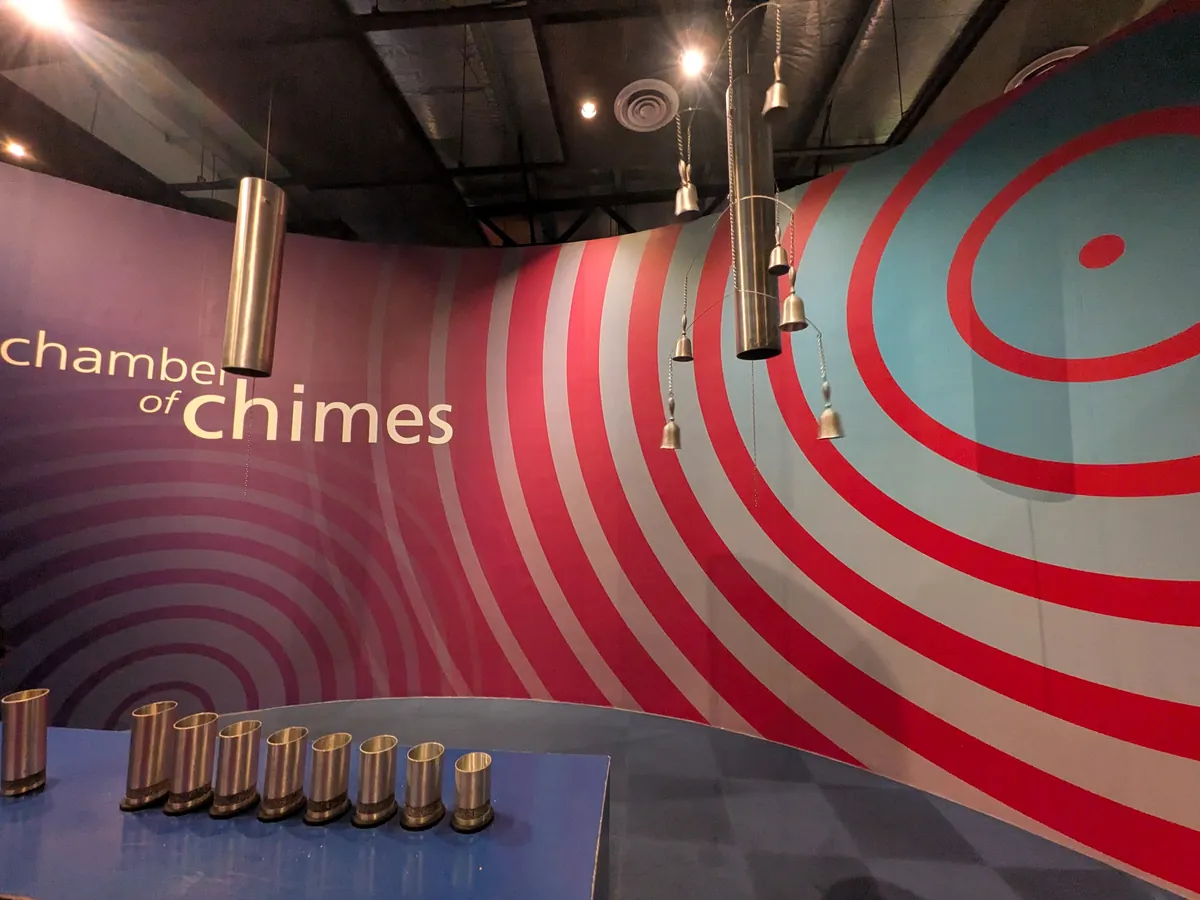 ピューターの管を吊るした体験展示 Chamber of Chimes。赤と青の同心円の壁