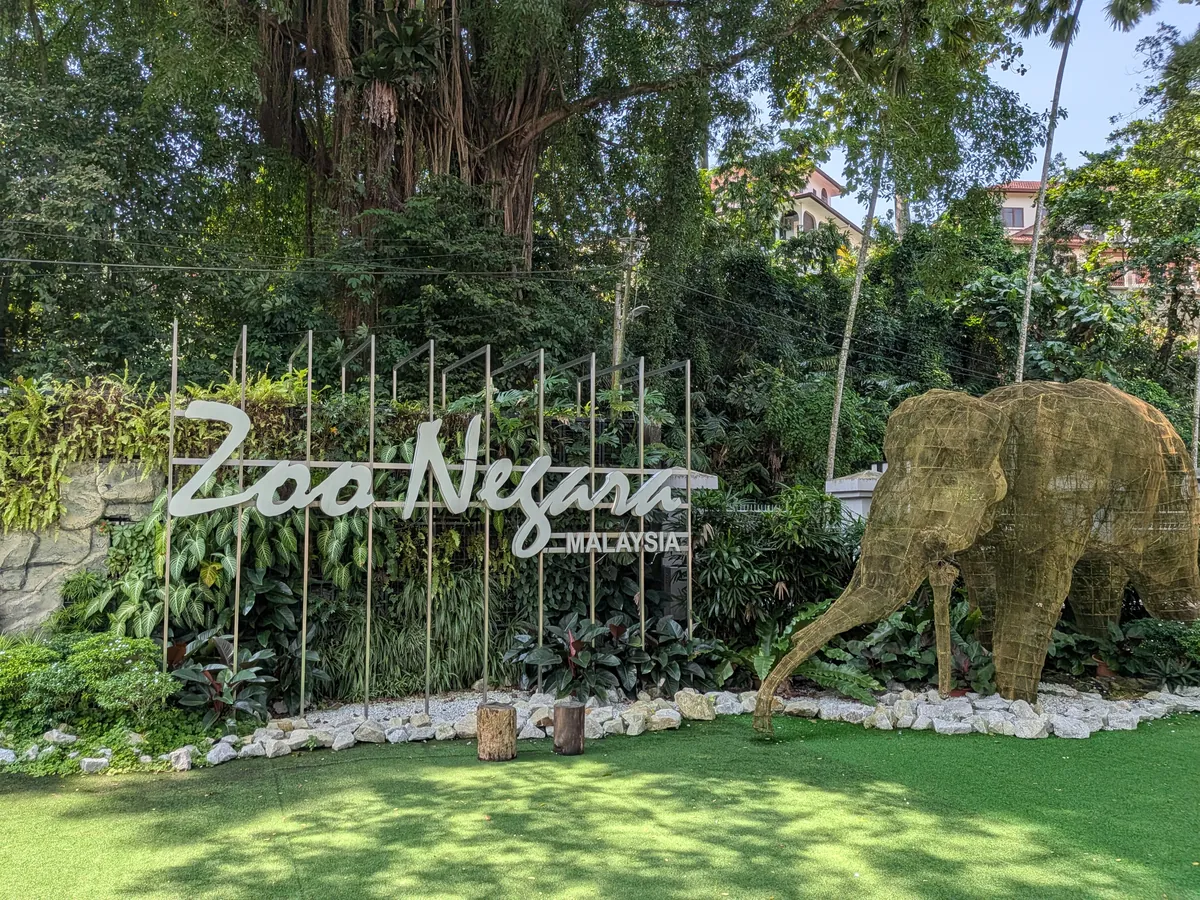 Zoo Negara Malaysia のサインと、枯れ草で作られた等身大の象のオブジェ