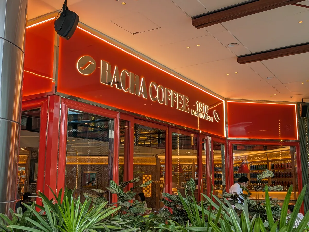 植栽越しに見たバチャコーヒー スリアKLCC店のオレンジと金の外観