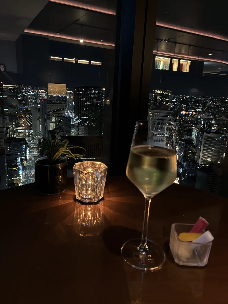 夜のラウンジ窓際。白ワインのグラスと大阪の夜景