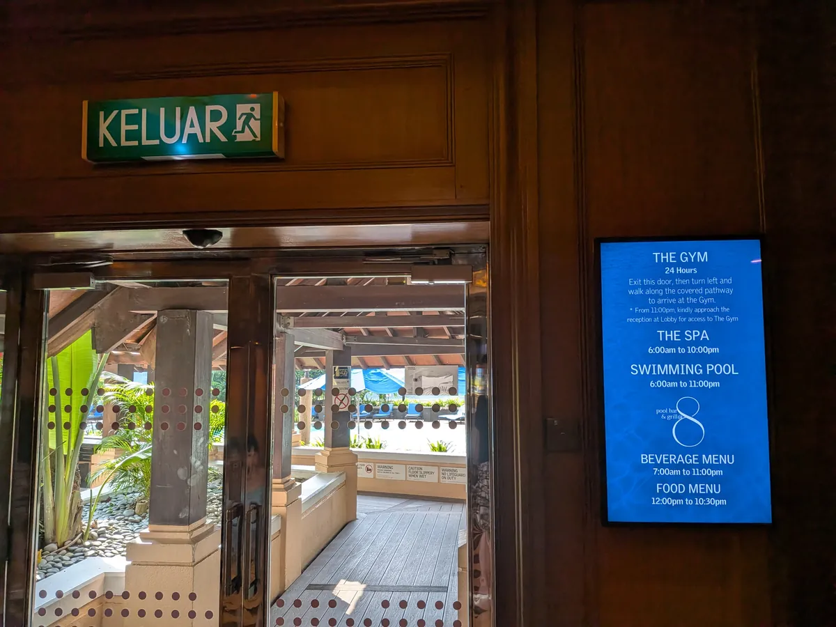 THE GYM・THE SPA・SWIMMING POOLの利用時間が表示されたデジタル案内板と出口