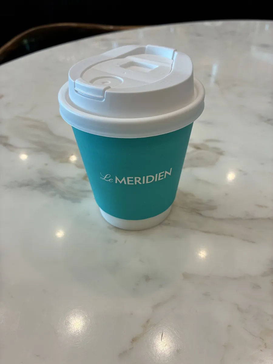 Le Meridienのロゴが入ったテイクアウトのコーヒーカップ。大理石のテーブルに置かれている