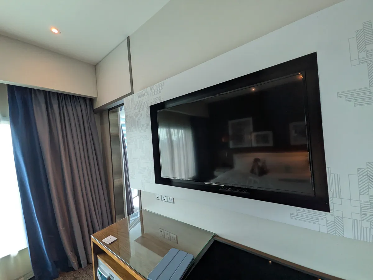 客室の壁掛けテレビと木製のキャビネット、窓のカーテン