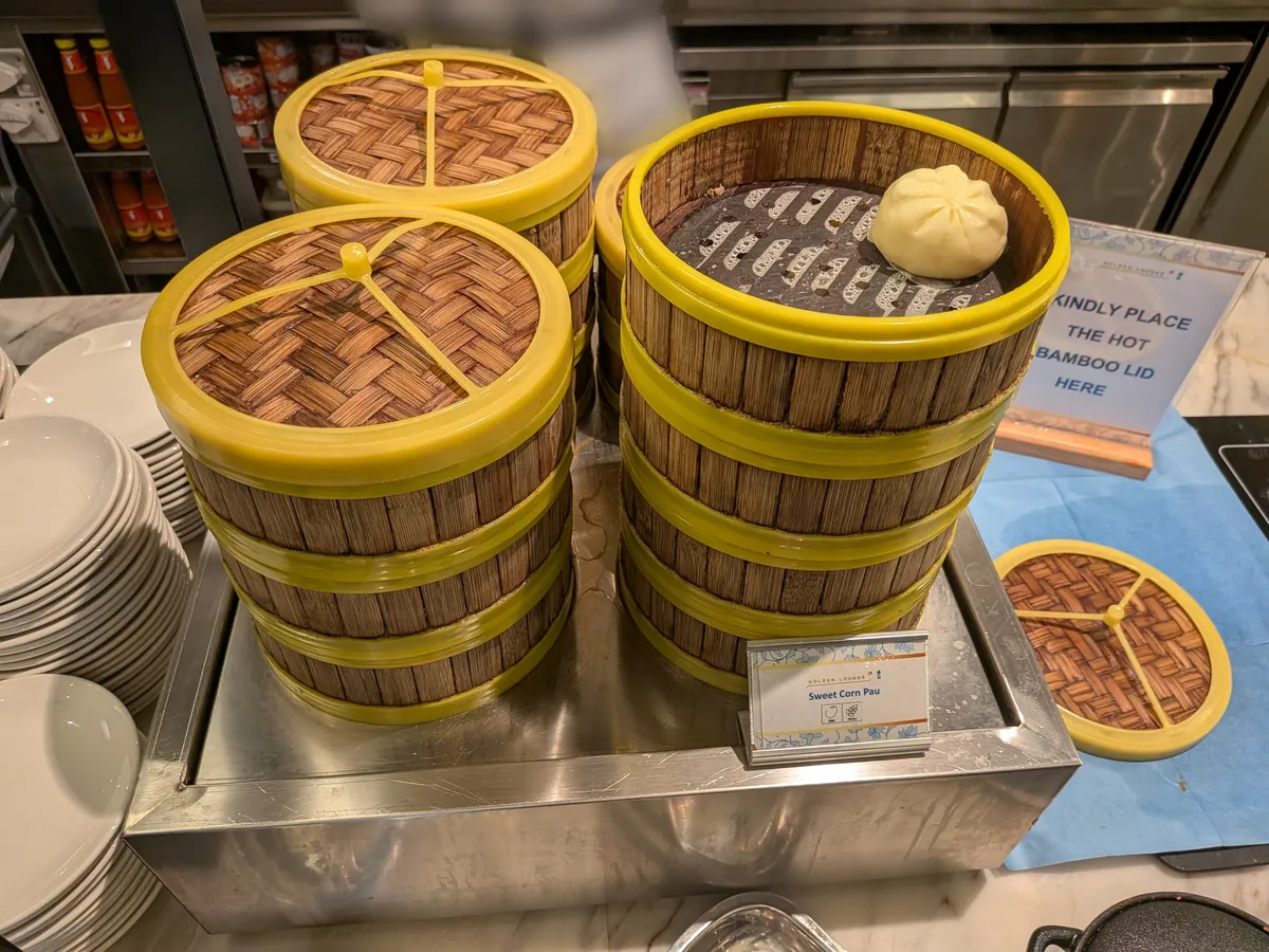 積み上げられた竹の蒸籠に入った点心のスイートコーン饅頭。「KINDLY PLACE THE HOT BAMBOO LID HERE」の案内も置かれている
