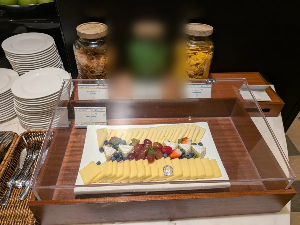 アクリルカバーの中のチーズプラッター。ハードチーズとブリーに、ぶどうとベリーが添えられている