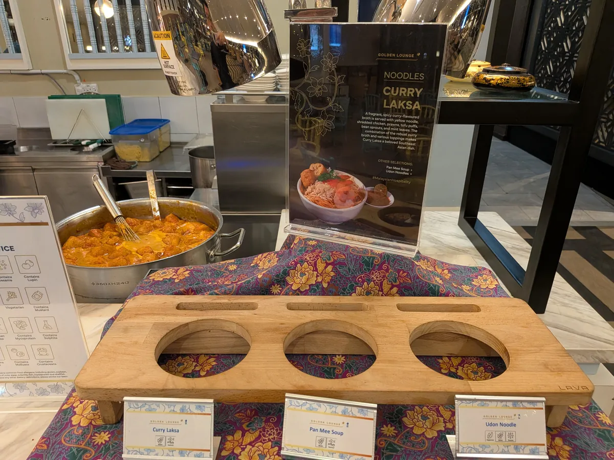 ライブヌードルバーのサイネージ「NOODLES CURRY LAKSA」と、Curry Laksa・Pan Mee Soup・Udon Noodle の3種を示す木製トレイ