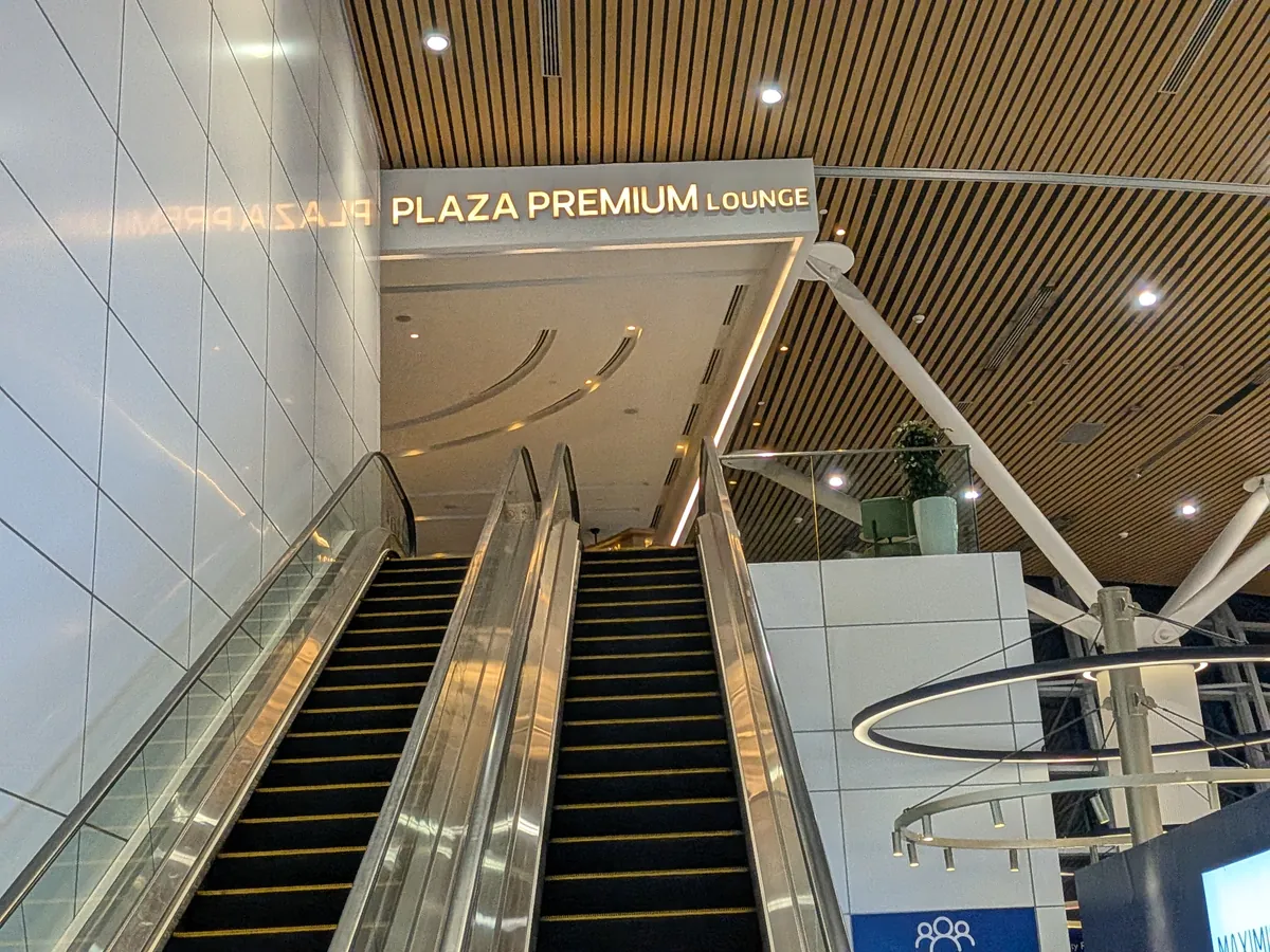 「PLAZA PREMIUM LOUNGE」の金文字サインとラウンジへ上がるエスカレーター。KLIA第1ターミナル コンタクトピアのメザニン階入口