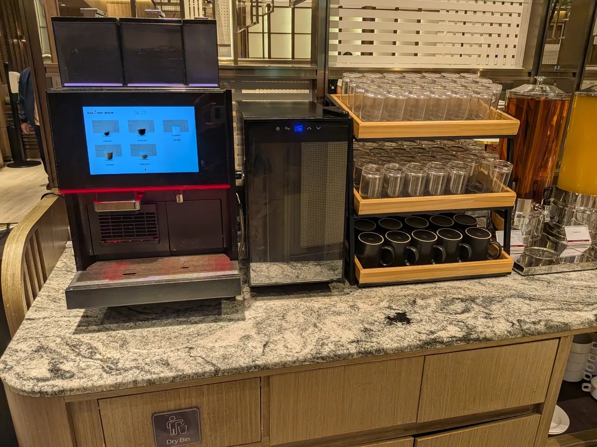 タッチパネル式のコーヒーマシンと、逆さに積まれたグラス・黒いカップのラック、奥に紅茶のディスペンサー