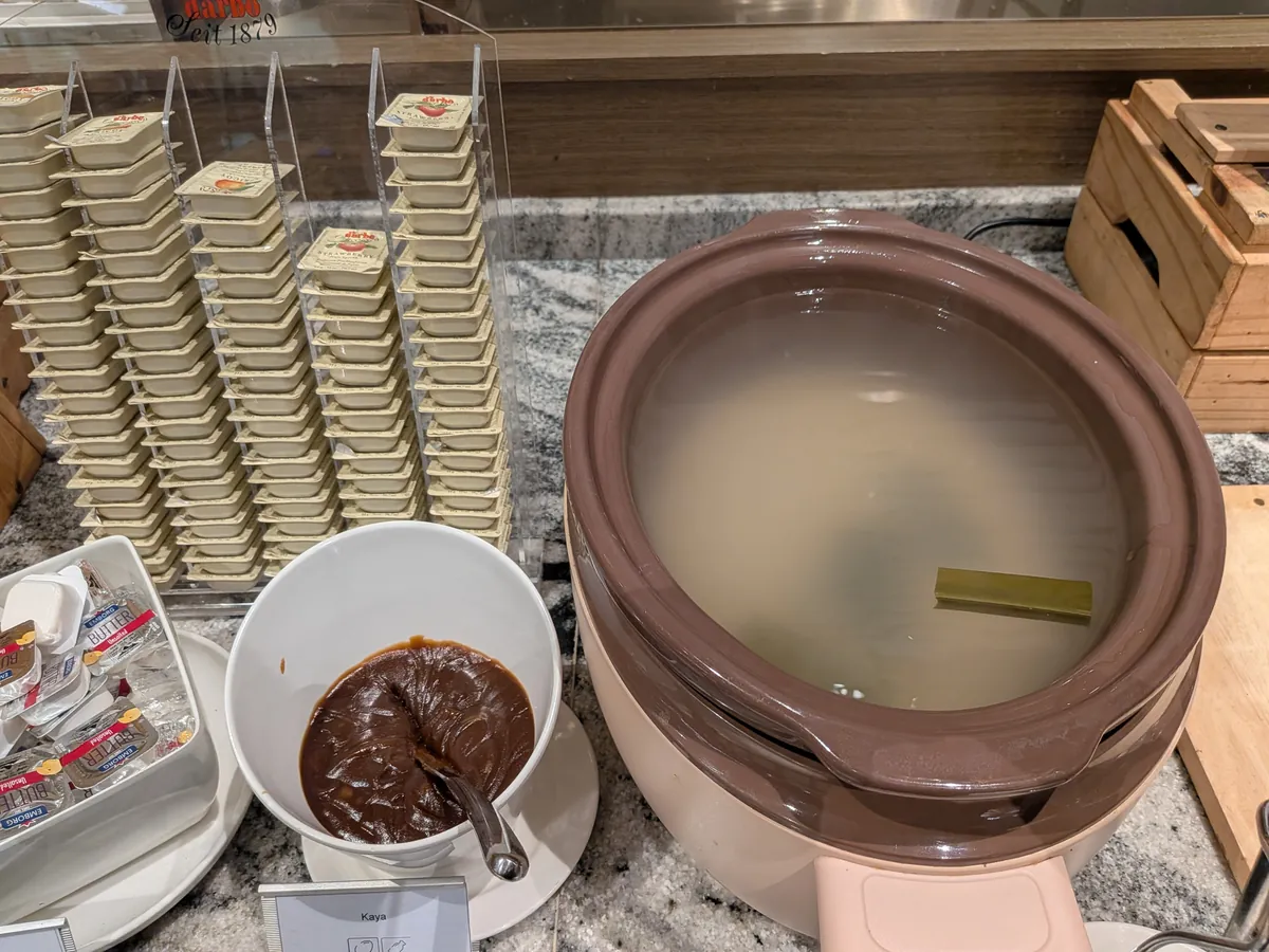 ココナッツと卵の甘いジャム「カヤ」が入った大きなボウルと、バターの小分けパック、積み上げられたヨーグルト、お粥の保温ジャー