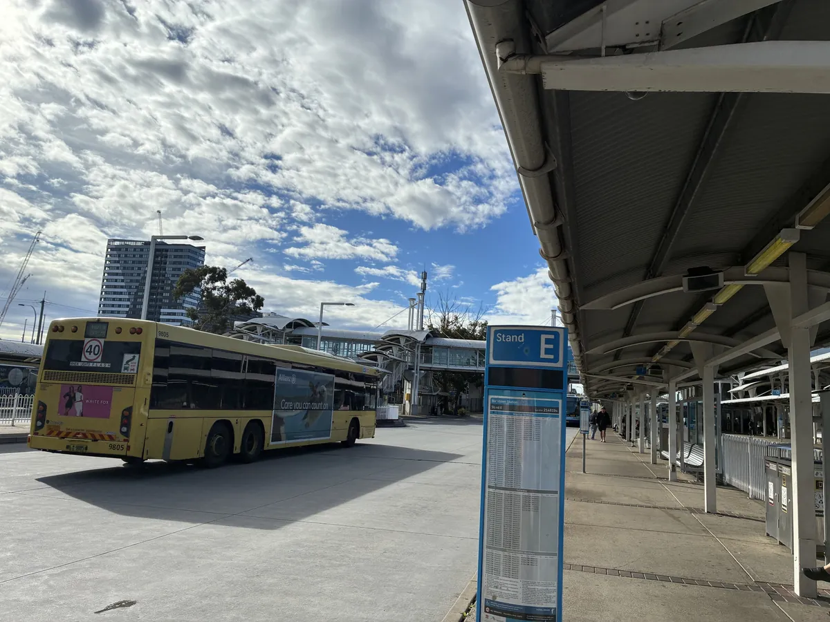 ブラックタウン駅のバスターミナル。黄色い路線バスが停車し、右手に「Stand E」の青い標識と屋根つきの待合スペースが続いている