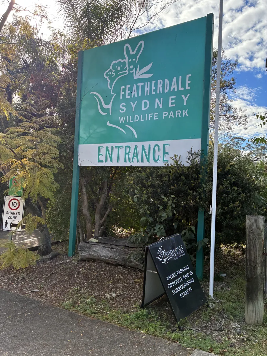 フェザーデール・シドニー・ワイルドライフパークの入口看板。緑地に白でコアラとカンガルーのイラストと「ENTRANCE」の文字が入っている