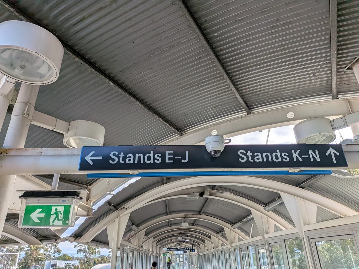 連絡通路に吊るされた案内板。「Stands E-J」が左矢印、「Stands K-N」が上矢印で示されている