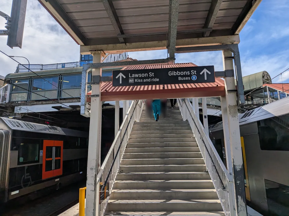 ブラックタウン駅の跨線橋。「Lawson St」「Gibbons St Buses B」の案内板が頭上に掲げられ、階段の下にシドニー・トレインズの車両が停車している