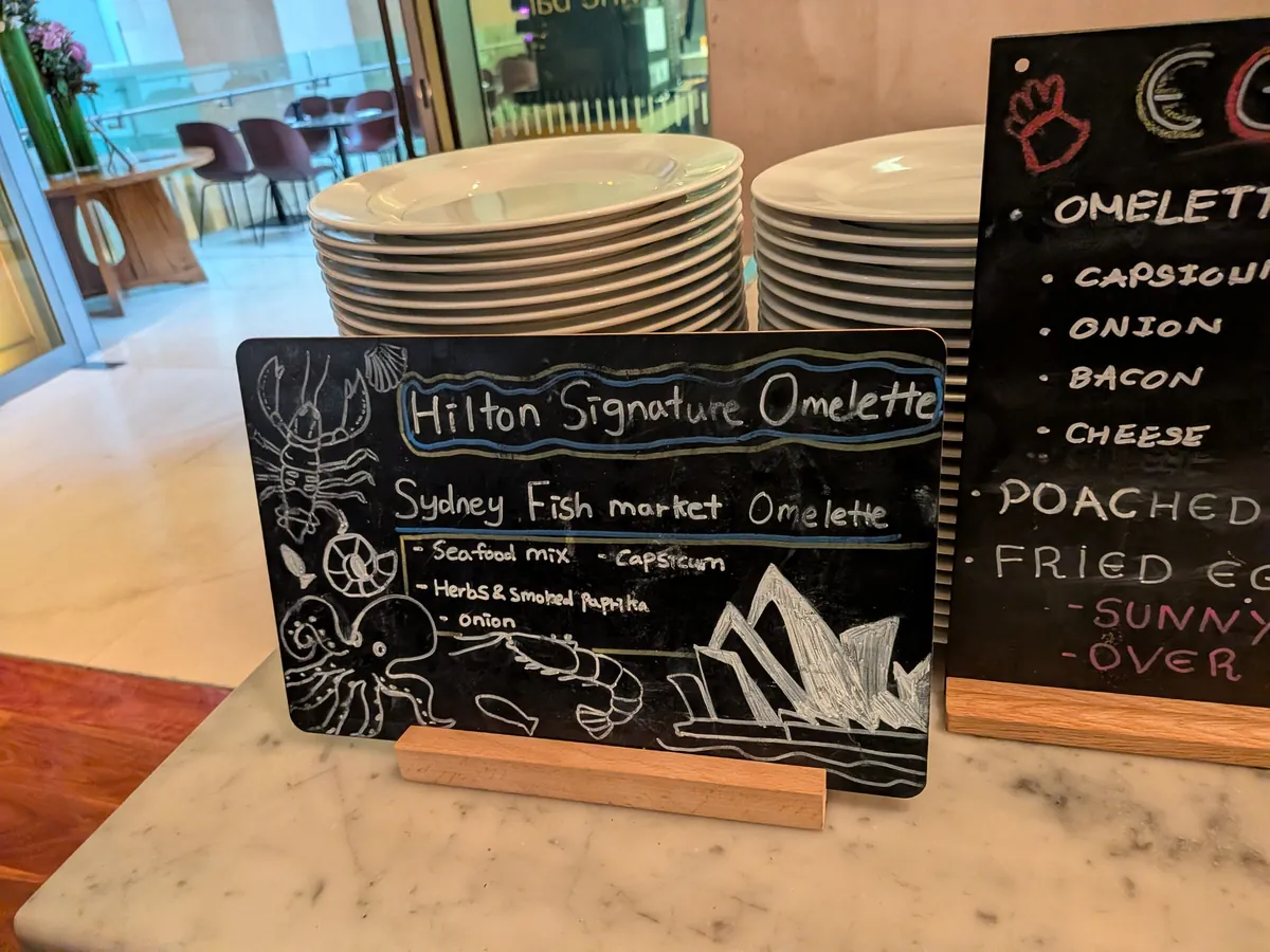 「Hilton Signature Omelette — Sydney Fish Market Omelette」の黒板。エビとロブスターのイラスト入り
