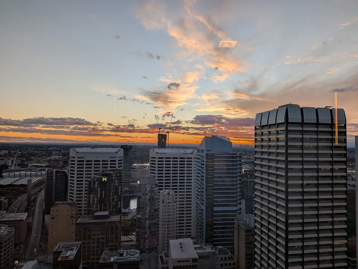 客室の窓から見たシドニー市街の夕景。ビルの向こうがオレンジに染まる