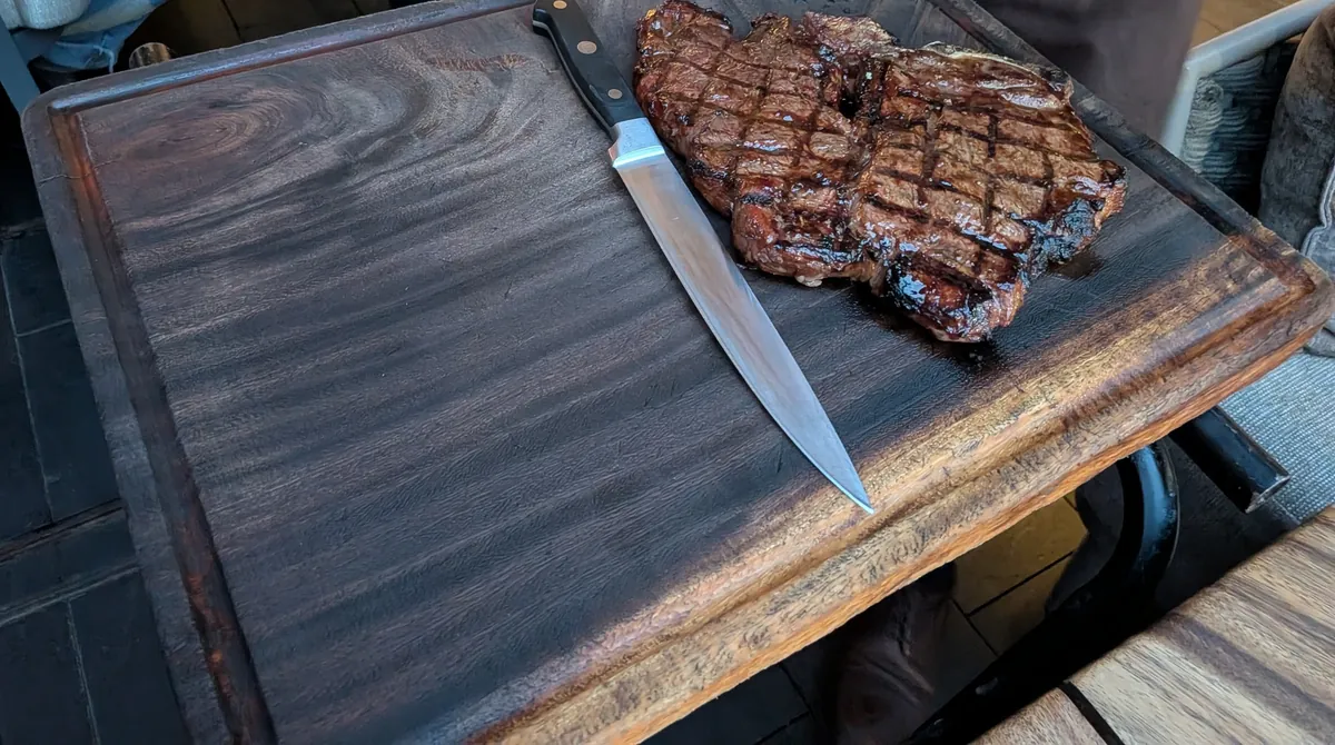 焼き上がったTボーンステーキが木のボードに載せられ、ナイフが添えられている。格子状の焼き目がついている