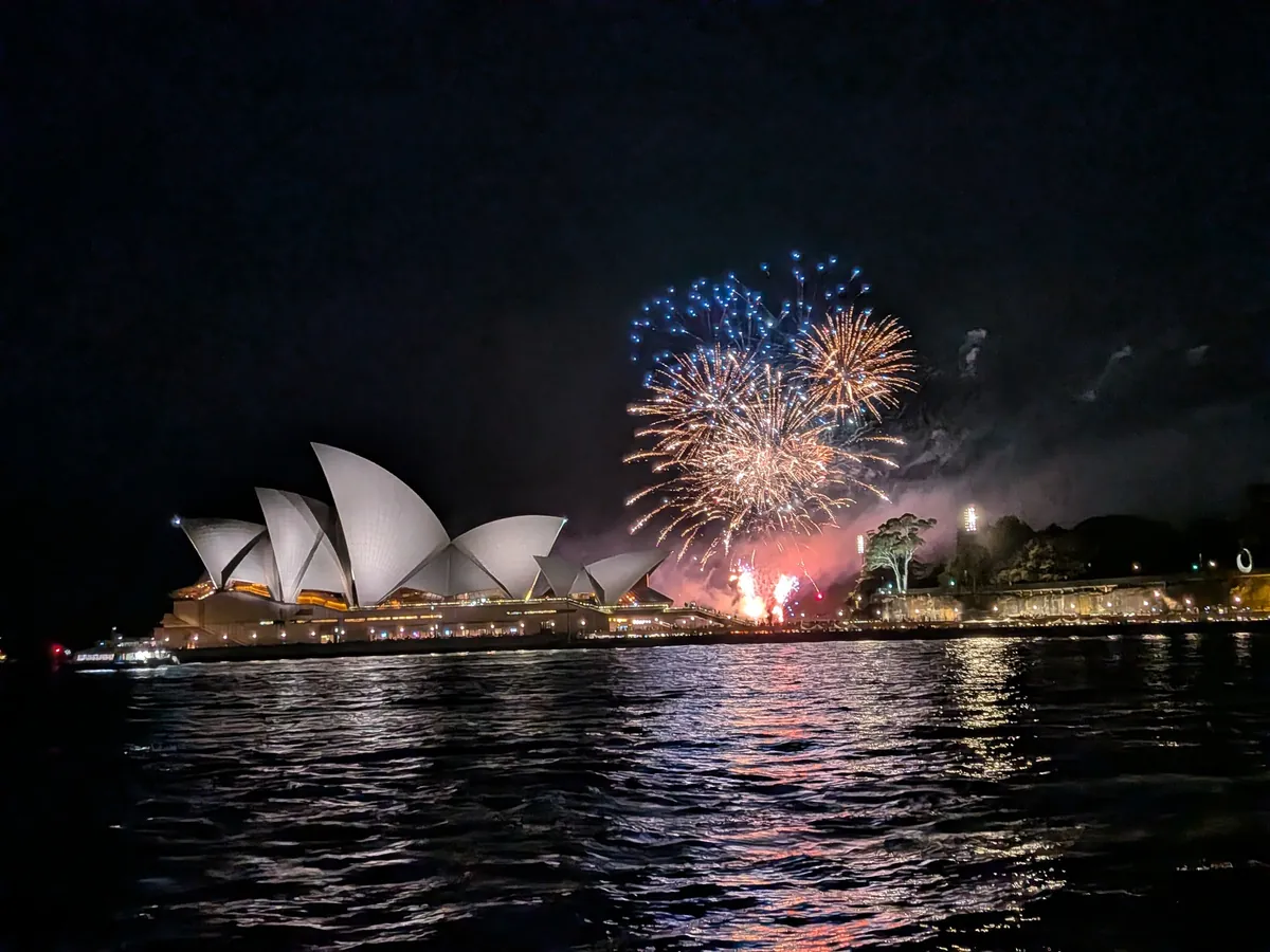 シドニー・オペラハウスのすぐ横の対岸に上がった花火。夜の海面に光が映り込んでいる