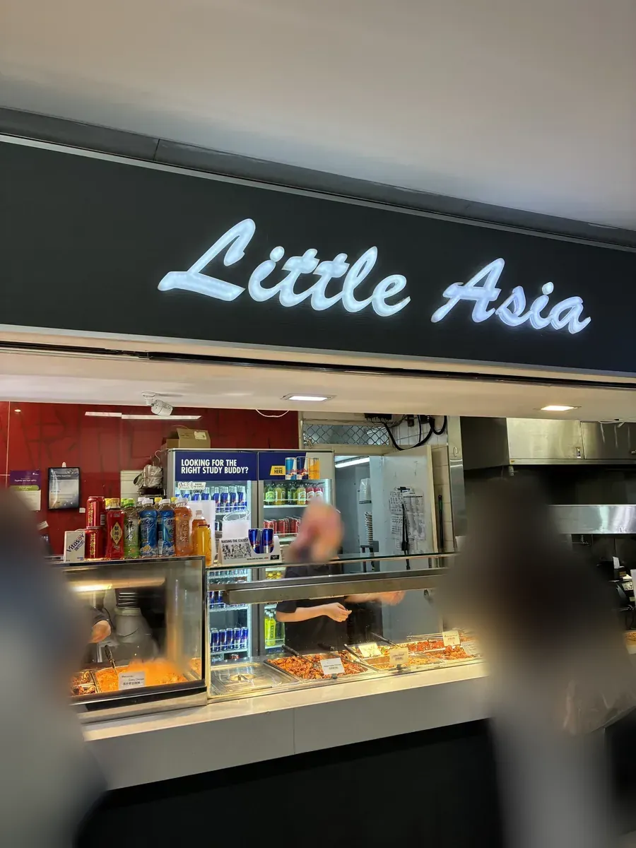 フードコート内のLittle Asiaの店構え。黒い壁に白い筆記体のネオンサインが光り、下に惣菜のショーケースが並ぶ
