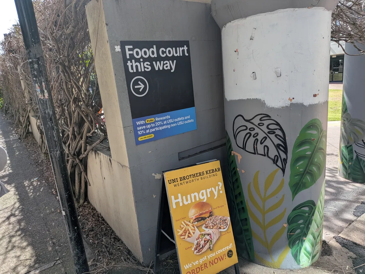キャンパスに立つ「Food court this way」の案内看板。下にUSU Rewardsで最大20%オフと書かれた青い案内が貼られている