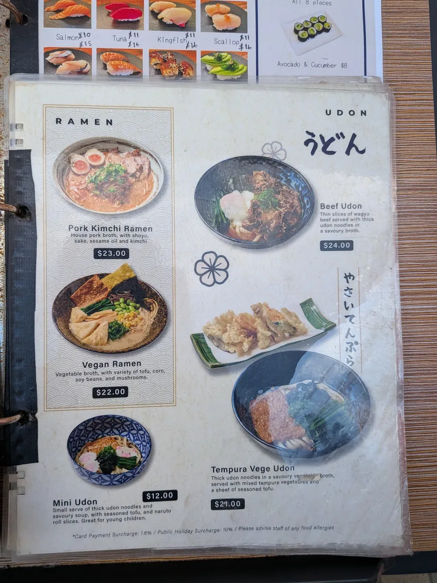 同じ店のラーメンとうどんのメニュー。ポークキムチラーメン23豪ドル、ビーフうどん24豪ドル、ミニうどん12豪ドルなどの価格が見える