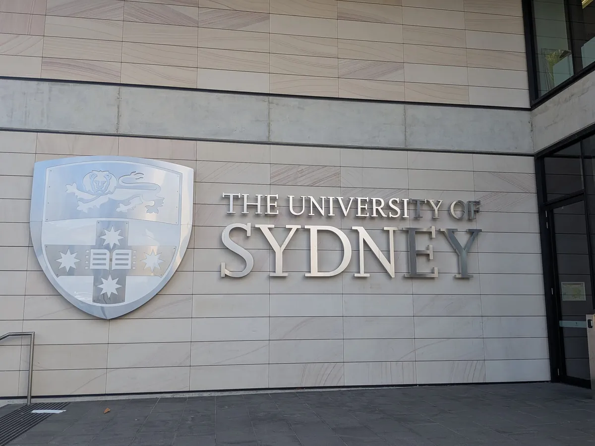 石張りの壁に掲げられたシドニー大学の紋章と「THE UNIVERSITY OF SYDNEY」の金属文字