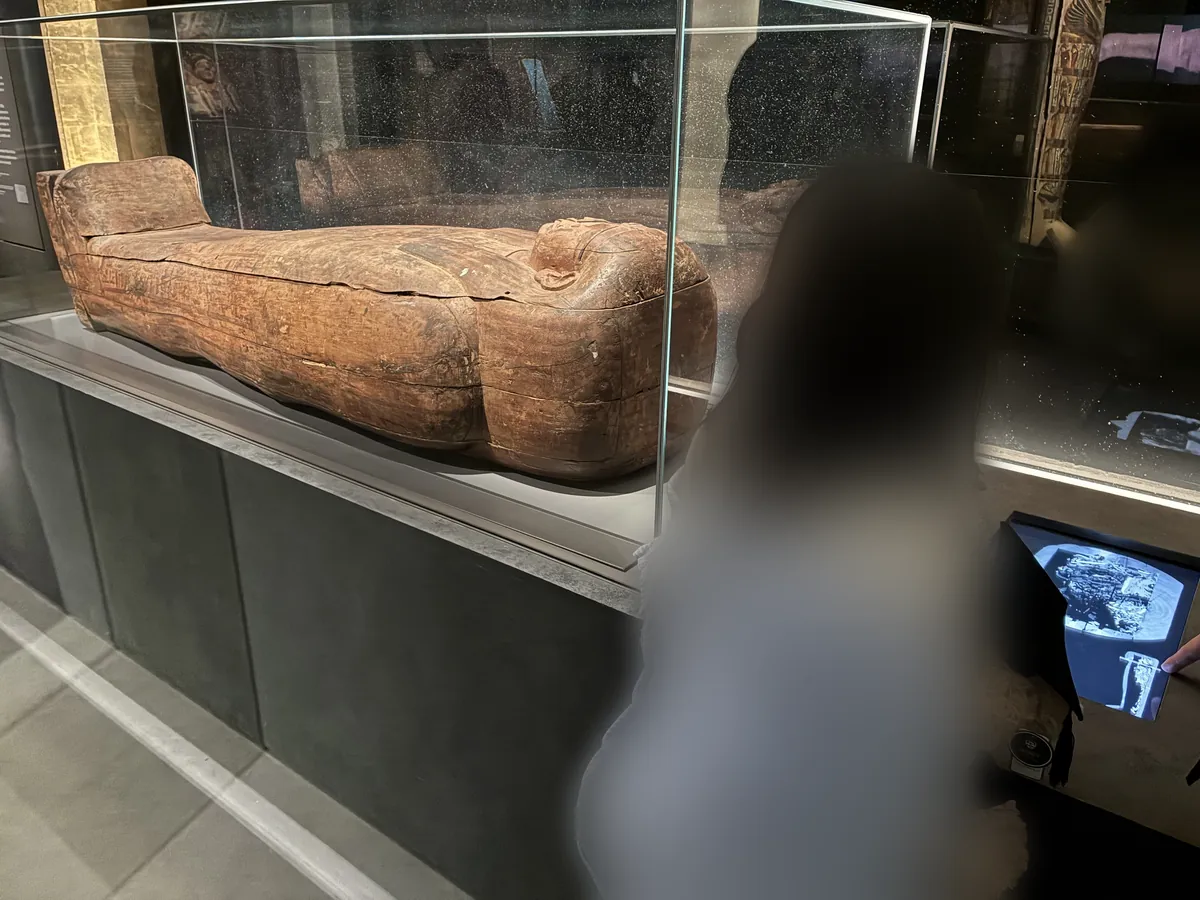 ガラスケースに横たわる古代エジプトの木の棺。右手に断層撮影の画像を映すタッチパネルが設置されている