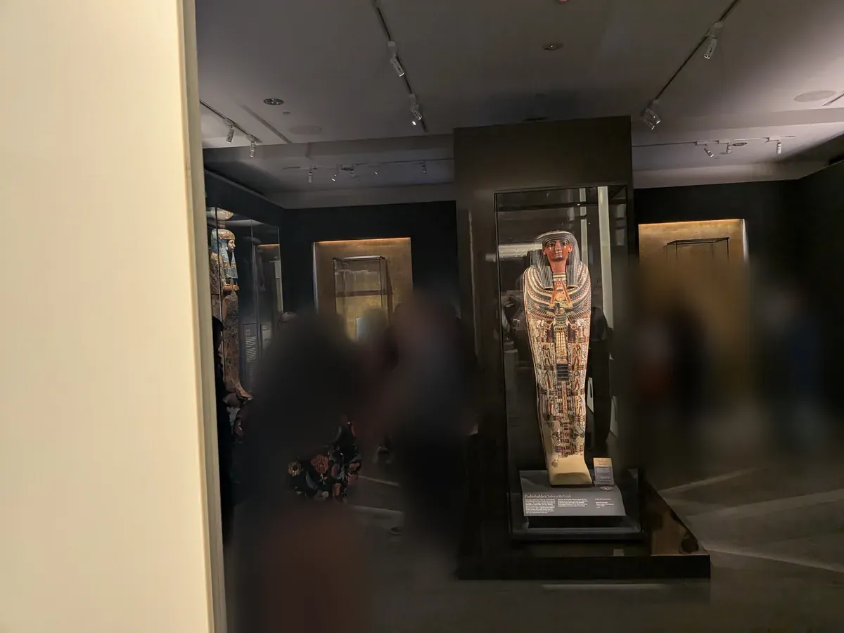 照明を落としたエジプトの展示室。奥のガラスケースに人型の棺が立てられ、金色の背景がスポットで照らされている