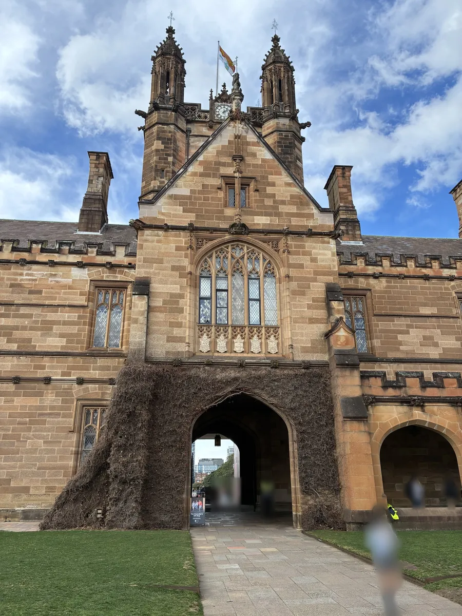シドニー大学クアドラングルの時計塔とメインゲート。砂岩のゴシック様式の尖塔の下にアーチ型の門があり、壁を落葉したツタが覆っている