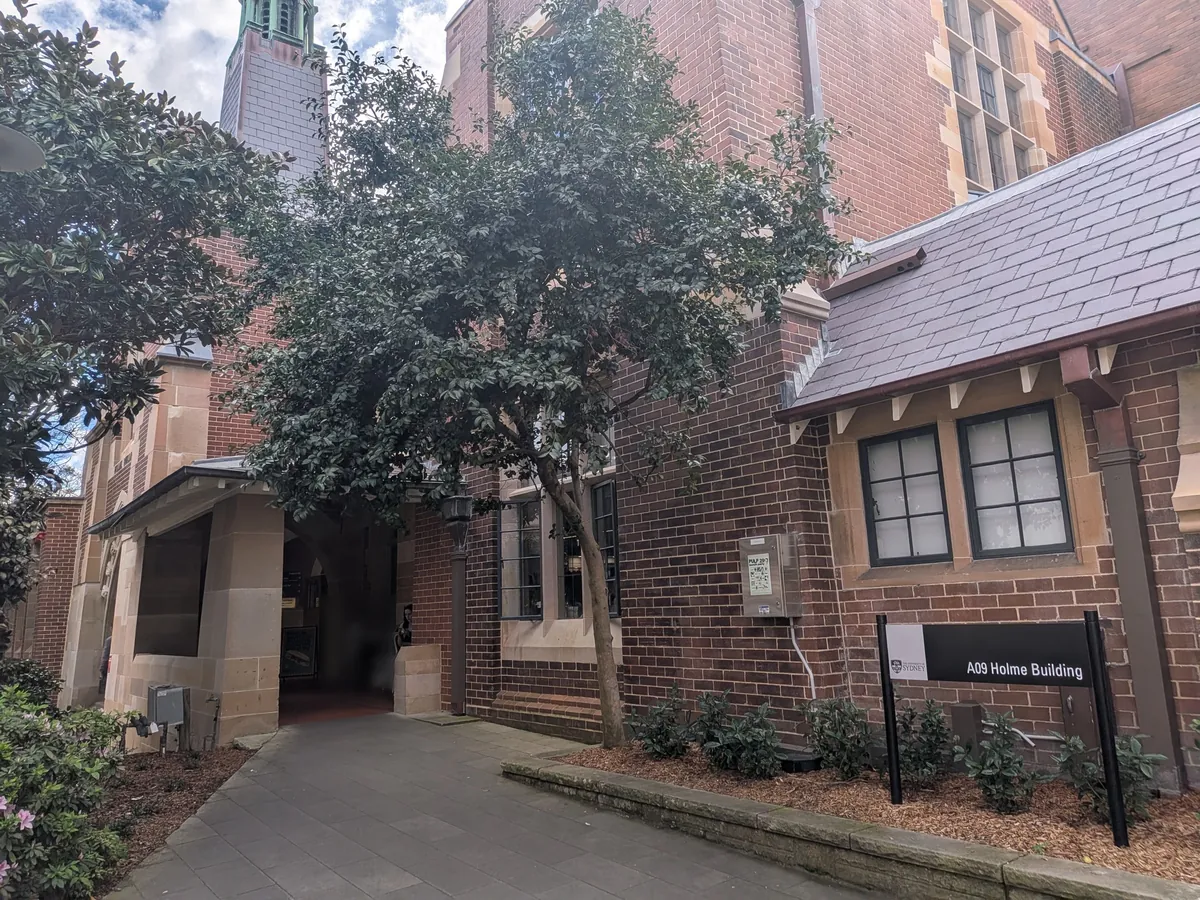 トンネルを抜けた先のレンガ造りの建物脇の小径。「A09 Holme Building」の表示板が立ち、奥に塔が見える