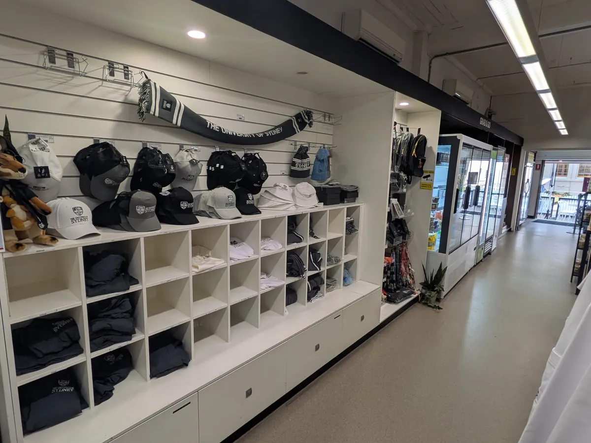 USYD Storeの店内。壁一面の棚に大学の紋章入りキャップが並び、たたまれたパーカーやTシャツが陳列されている